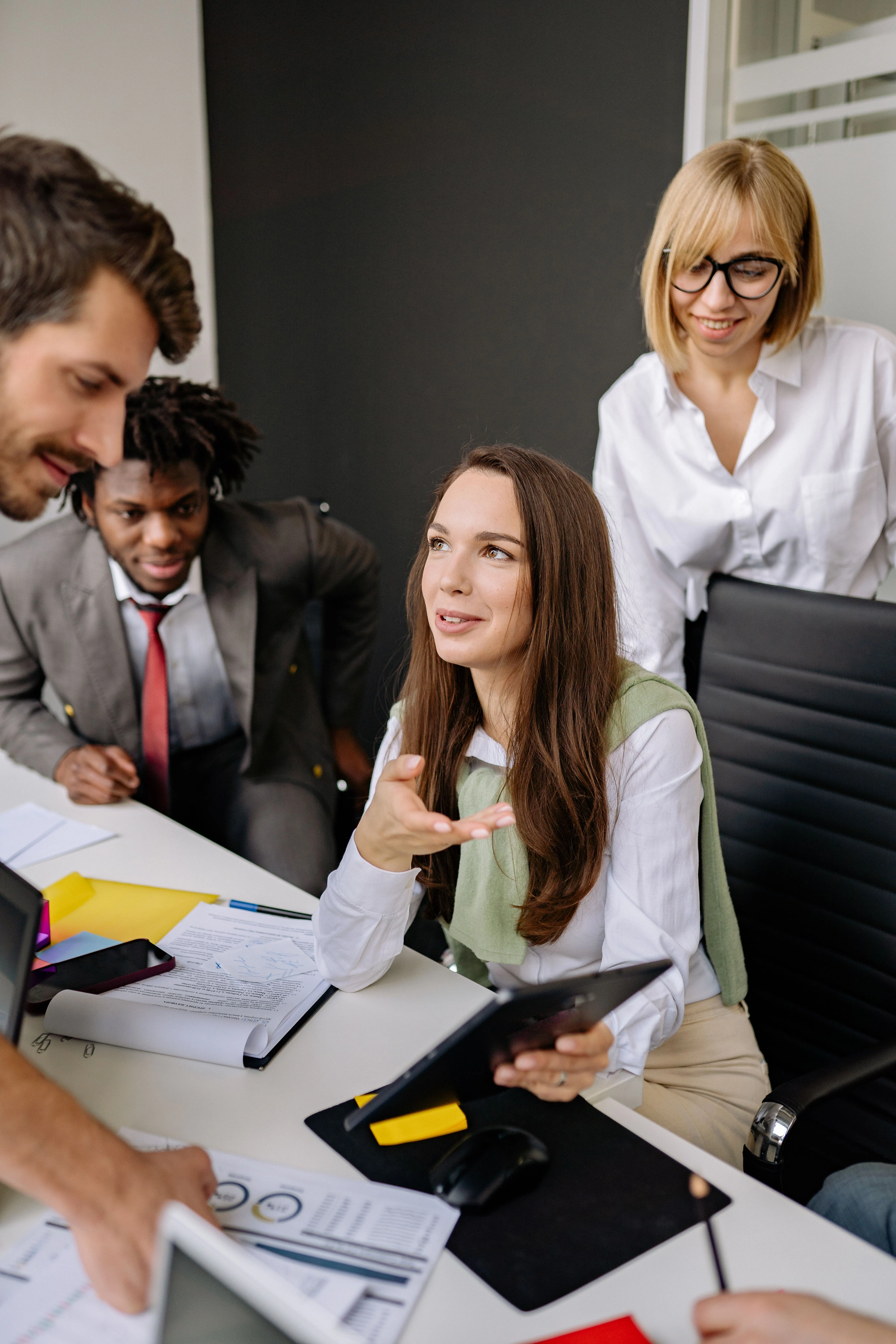 Profissionais conversando em equipe, reunidos ao redor de uma mesa de trabalho.